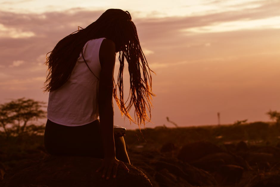 Silhouette of a woman sitting on rocks during a vibrant sunset in Lodwar, Kenya.
